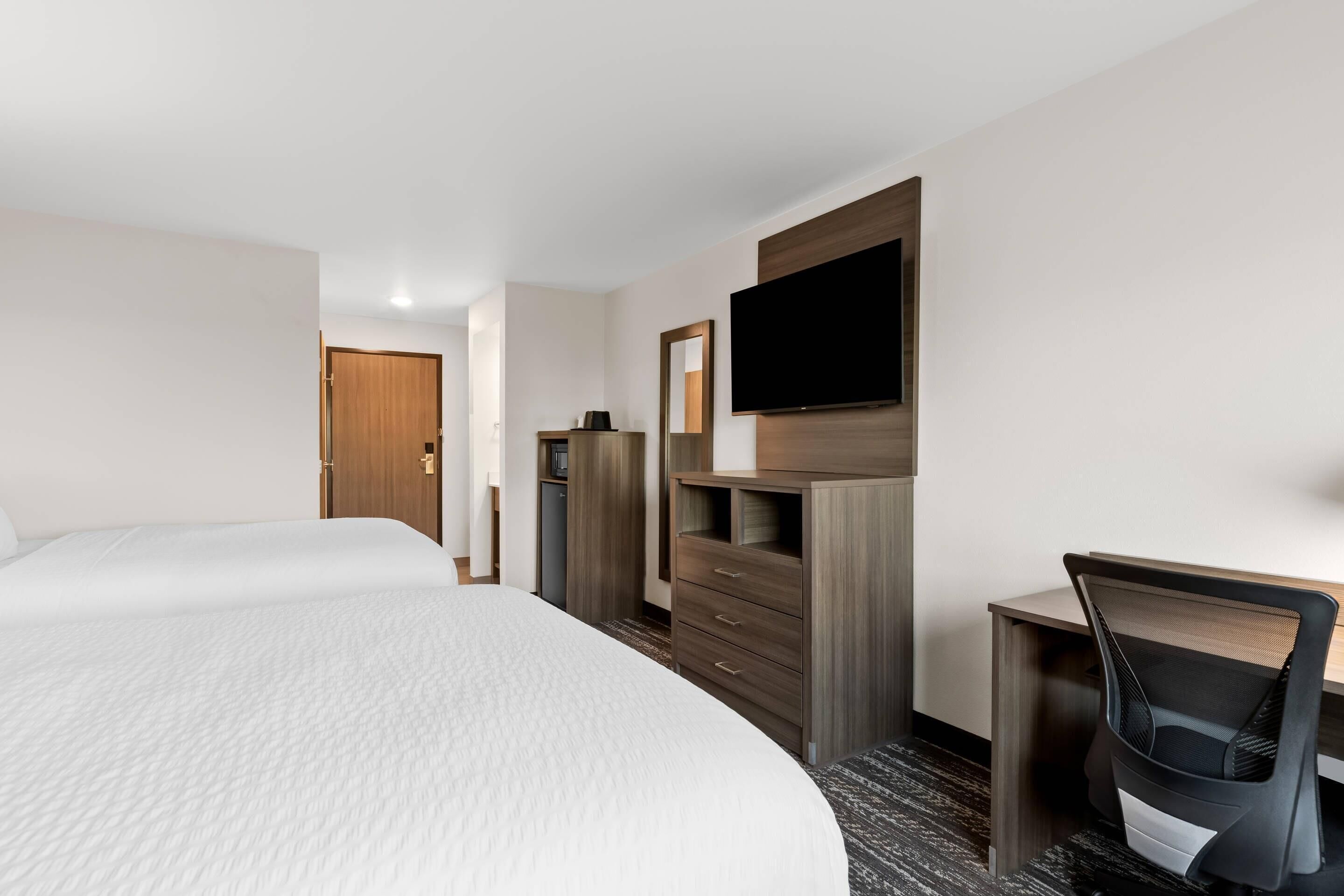 Una habitación de hotel con una cama grande, un escritorio con silla, un televisor en la pared y un armario.
