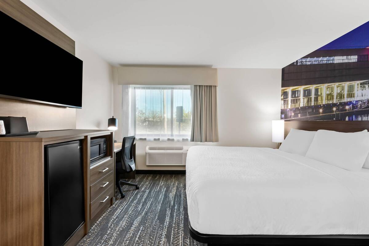 Hotelkamer met een groot bed, een flatscreen televisie, een bureau met een magnetron en een groot raam met gordijnen.