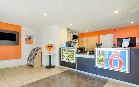 A reception area with a counter, a TV, a poster, and a small table with a vase of flowers.