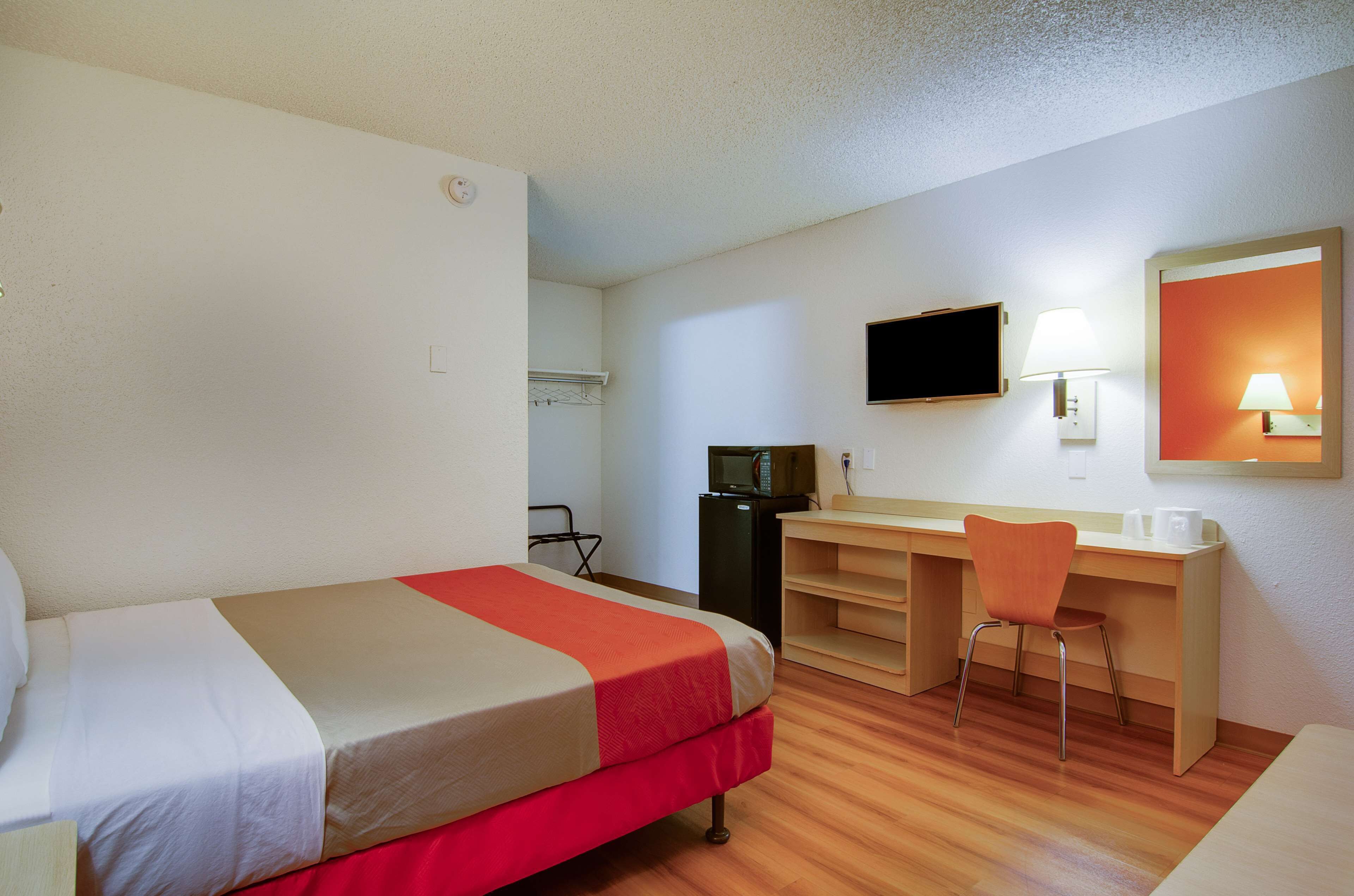 A hotel room with a bed, desk, chair, television, and a small kitchenette.