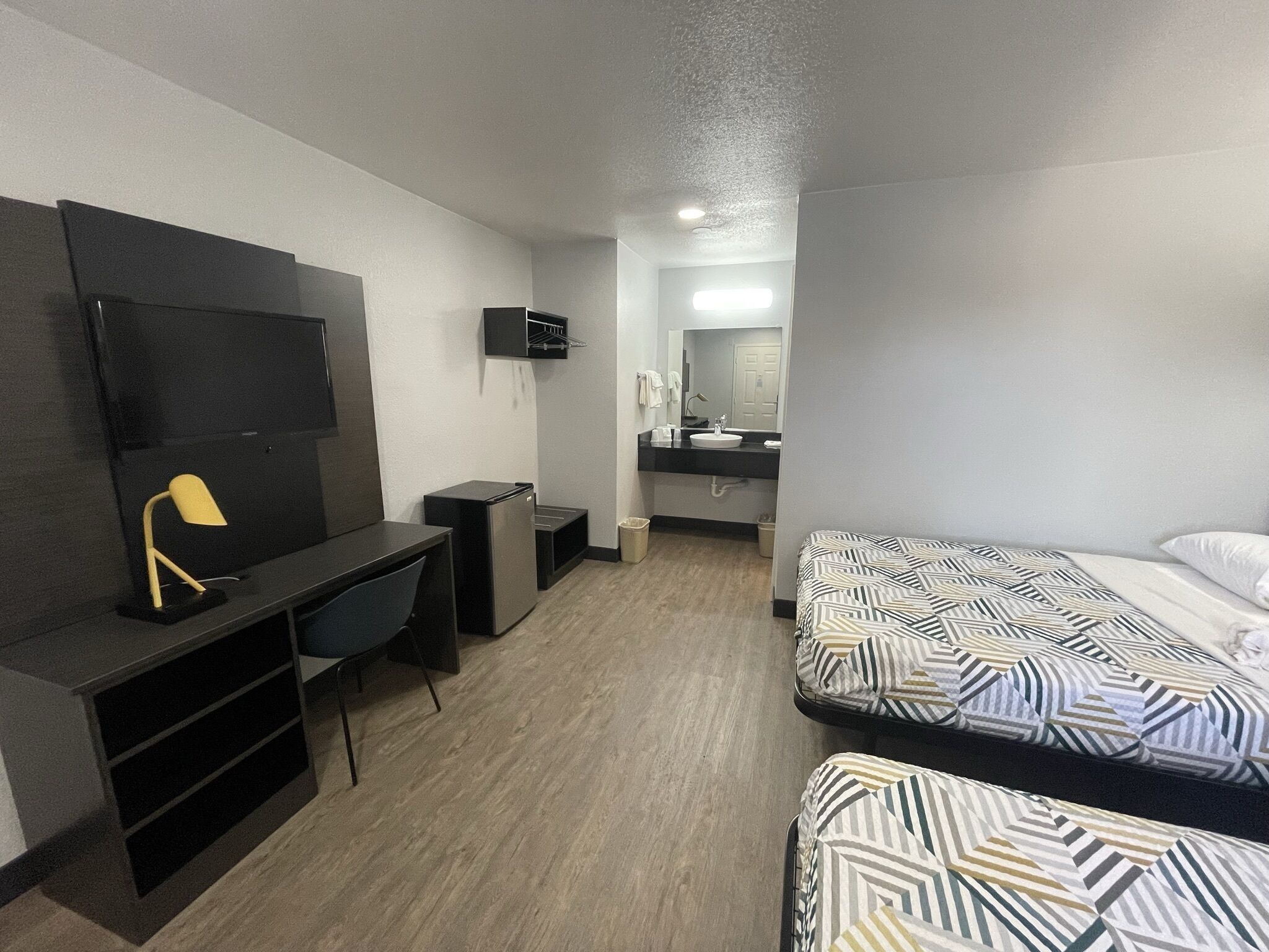 A hotel room with a desk, a TV, a bed with patterned bedding, and a bathroom with a mirror and sink.