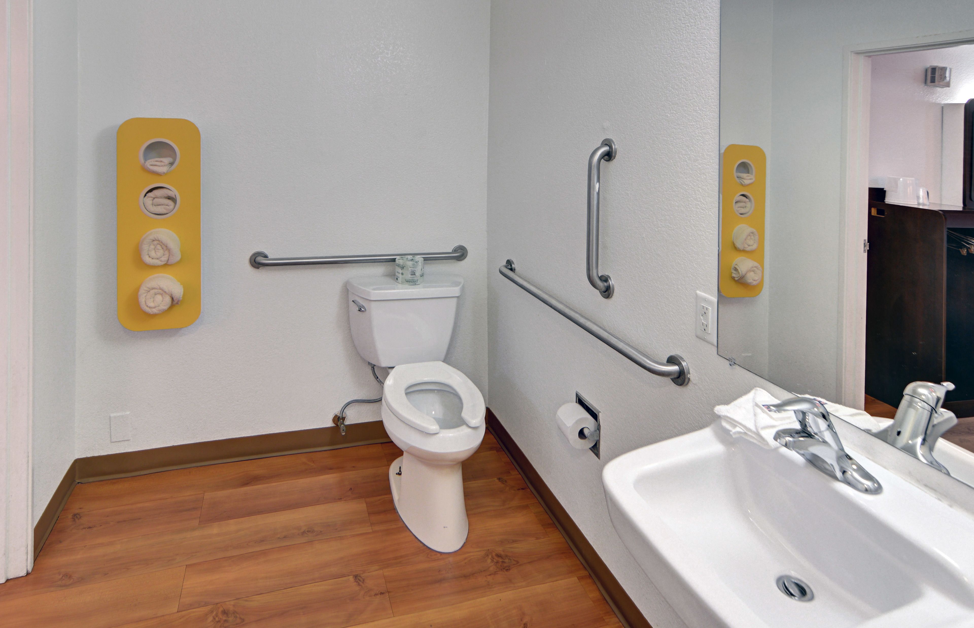 A bathroom with a white toilet, wooden flooring, a sink with a mirror, and a yellow towel rack.