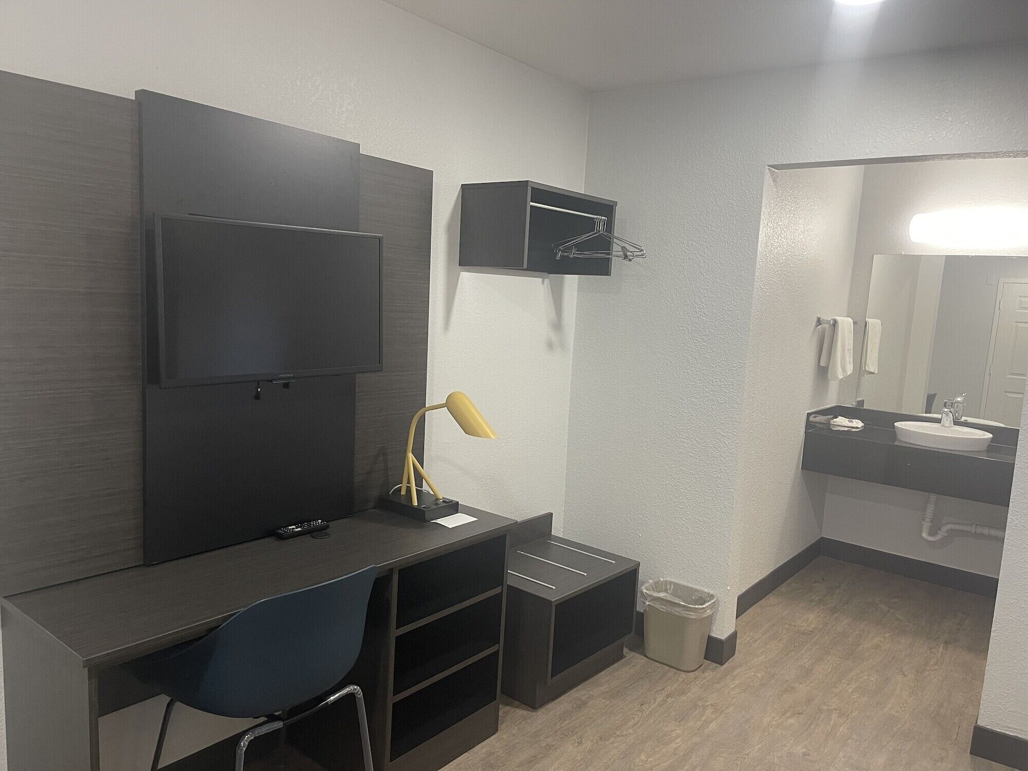 A modern bathroom with a dark wood vanity, a mounted TV, a small desk with a chair, and a sink with a mirror.