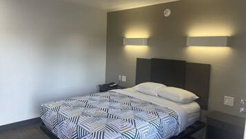 A hotel room with a bed, bedside table, and a wall-mounted light fixture.