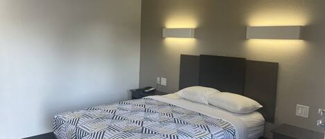 A hotel room with a bed, bedside table, and a wall-mounted light fixture.