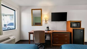 A hotel room with two beds, a desk with a chair, a TV, a lamp, a microwave, and a refrigerator.