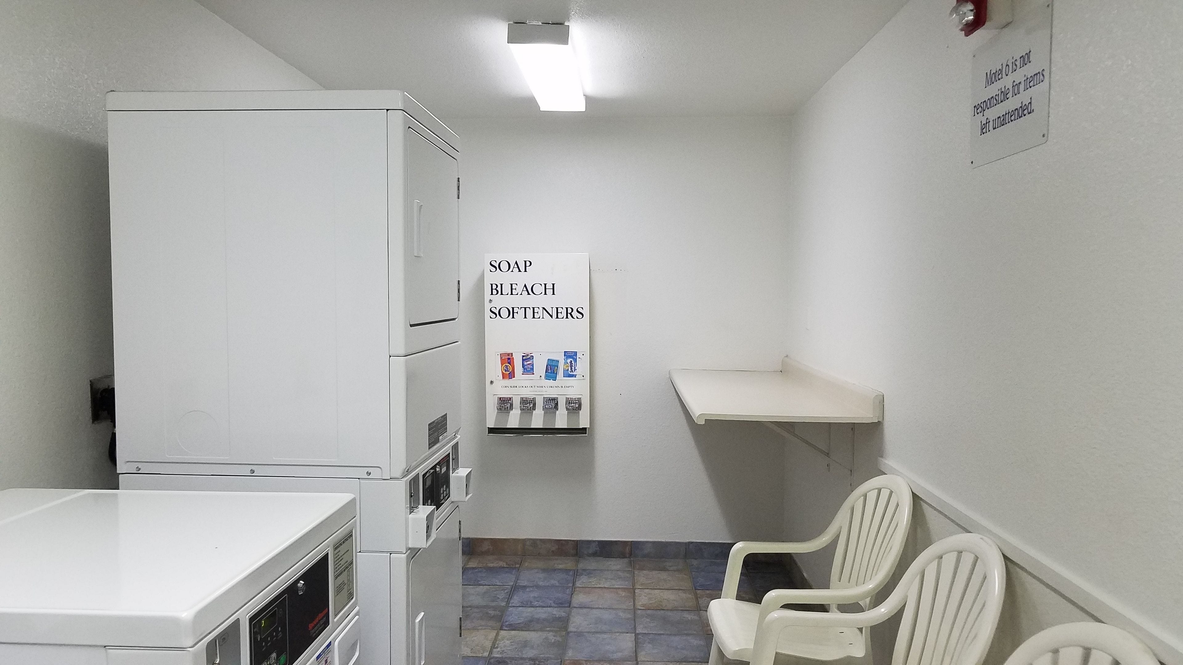 A small, clean room with a washing machine, a shelf with toiletries, and a chair.