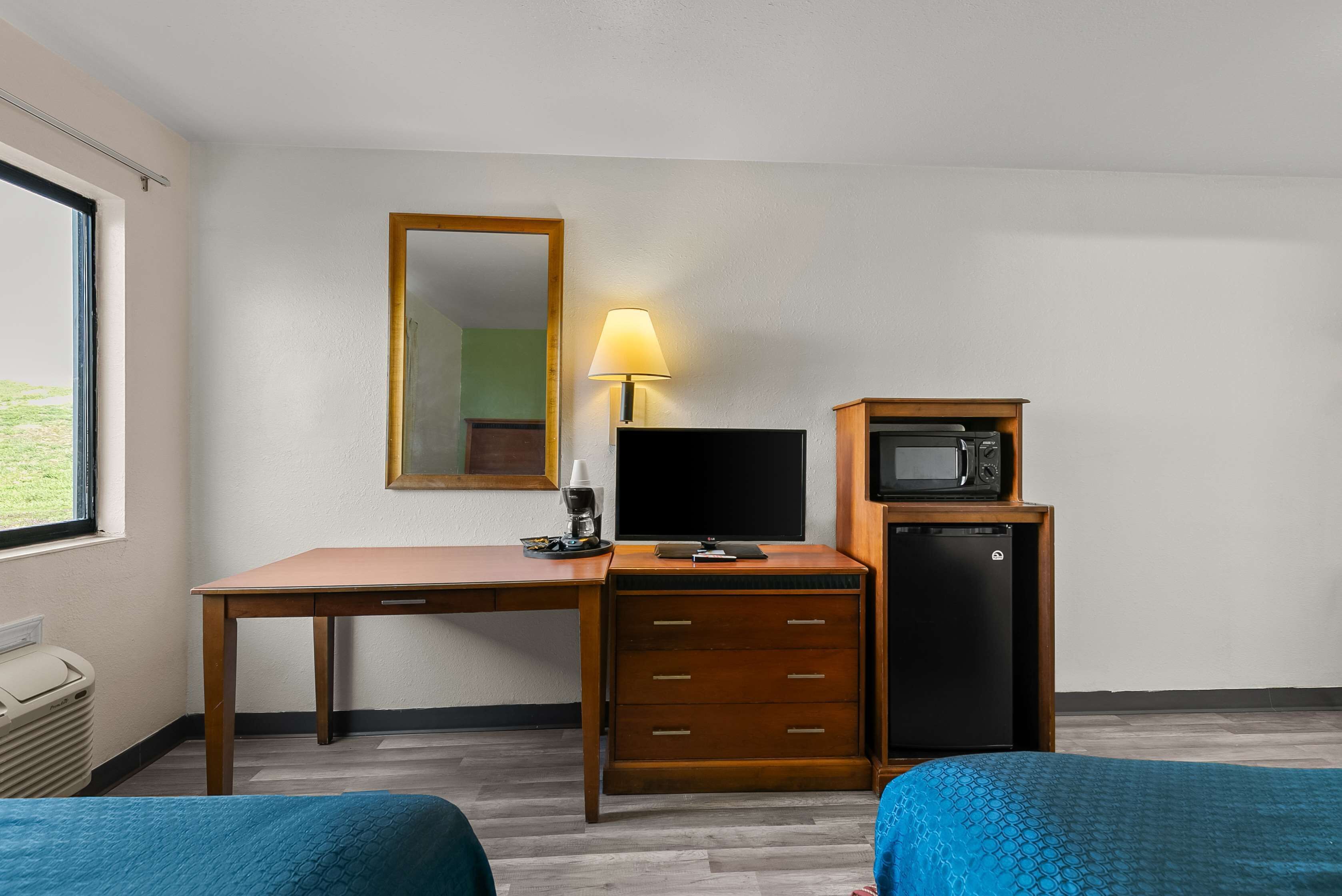Ein Hotelzimmer mit einem Holztisch, einem Fernseher, einer Mikrowelle, einer Lampe und zwei Betten.