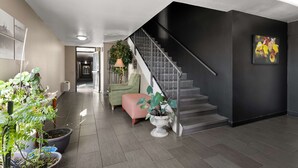 Een modern interieur met een trap, potplanten, een groene fauteuil en een kunstwerk in een lijst aan de muur.