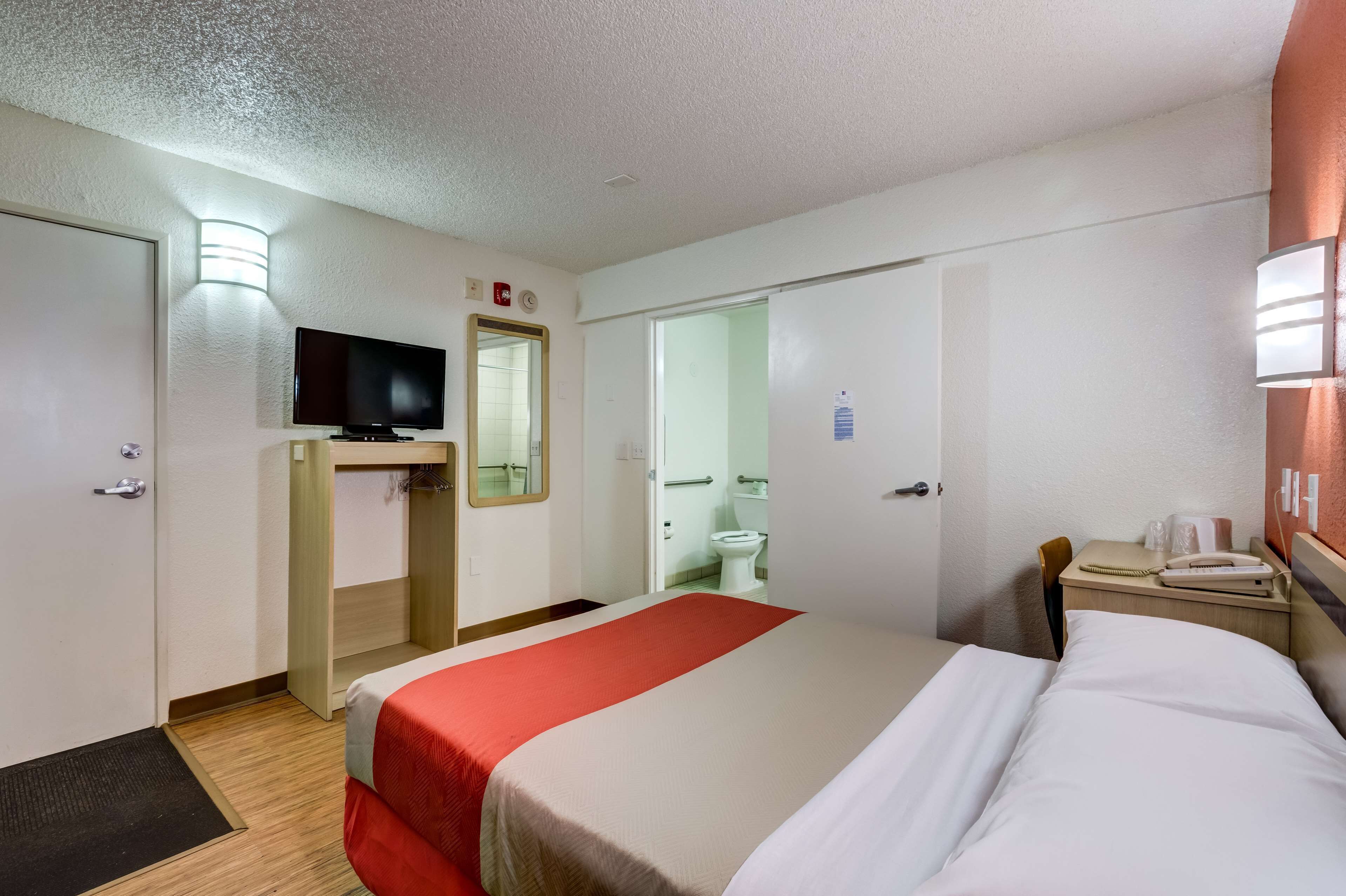 A hotel room with a bed, a television, a desk with a telephone, and a bathroom visible through an open door.
