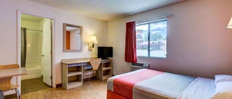 A hotel room with a bed, desk, chair, TV, and a window with curtains.