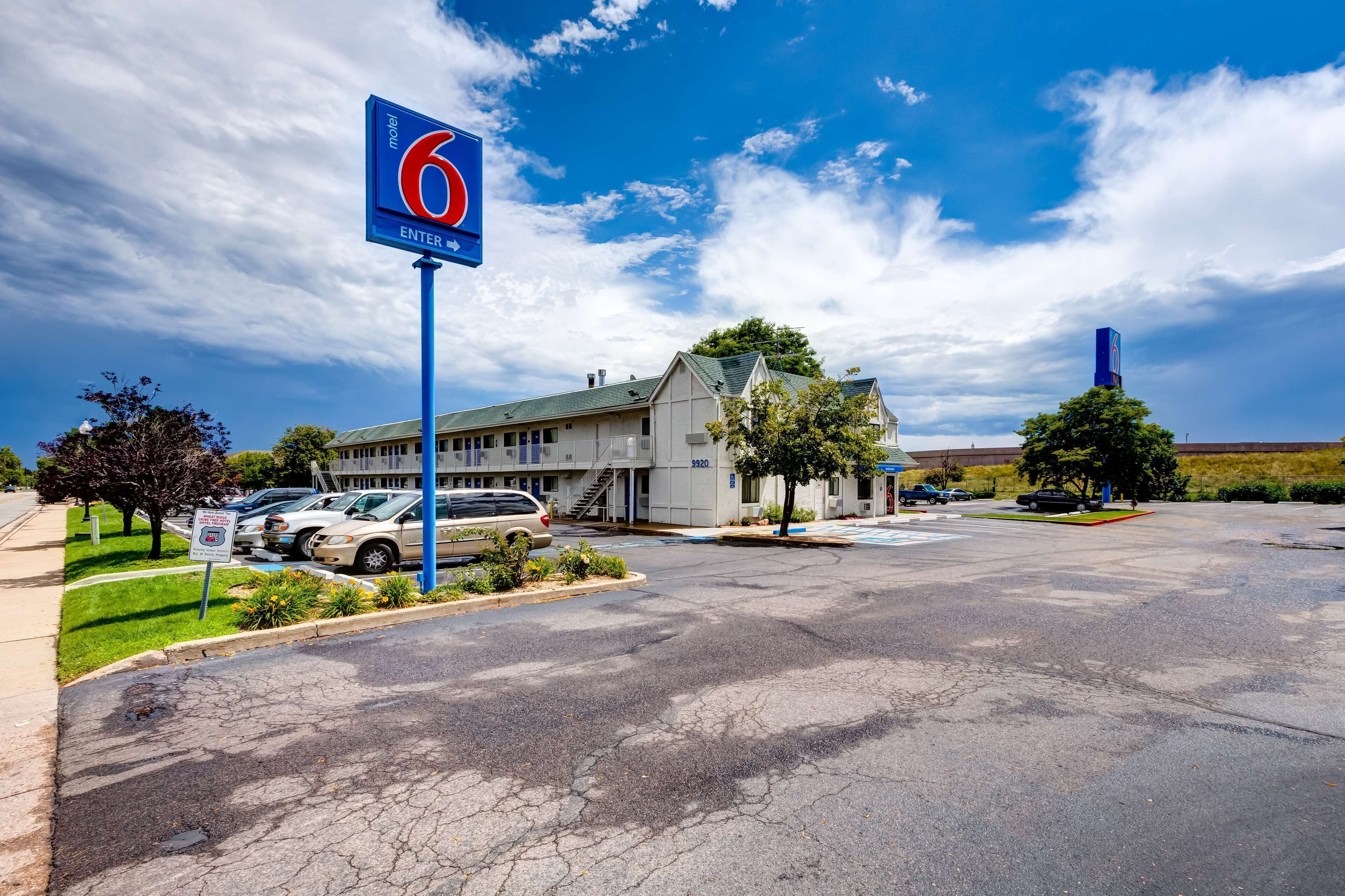 Un motel avec un grand panneau indiquant le chiffre « 6 », un parking et un bâtiment doté d’un toit vert.