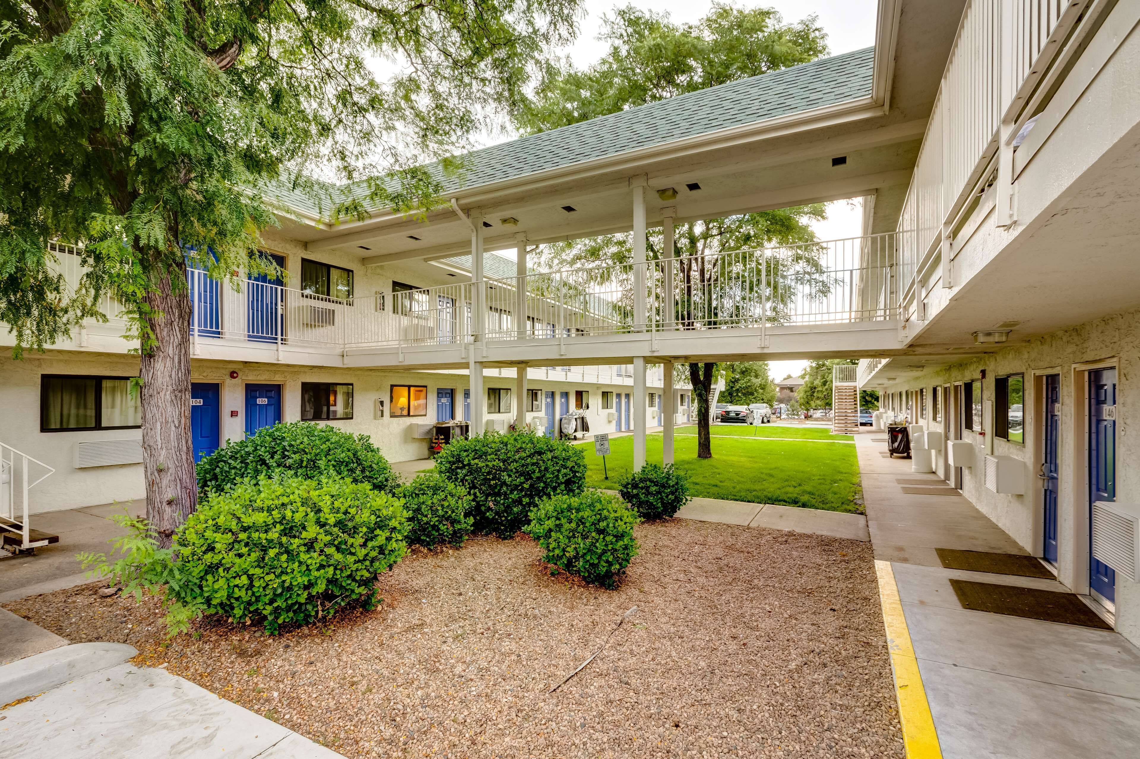 A motel with a covered walkway, multiple rooms with blue doors, and a small lawn area.