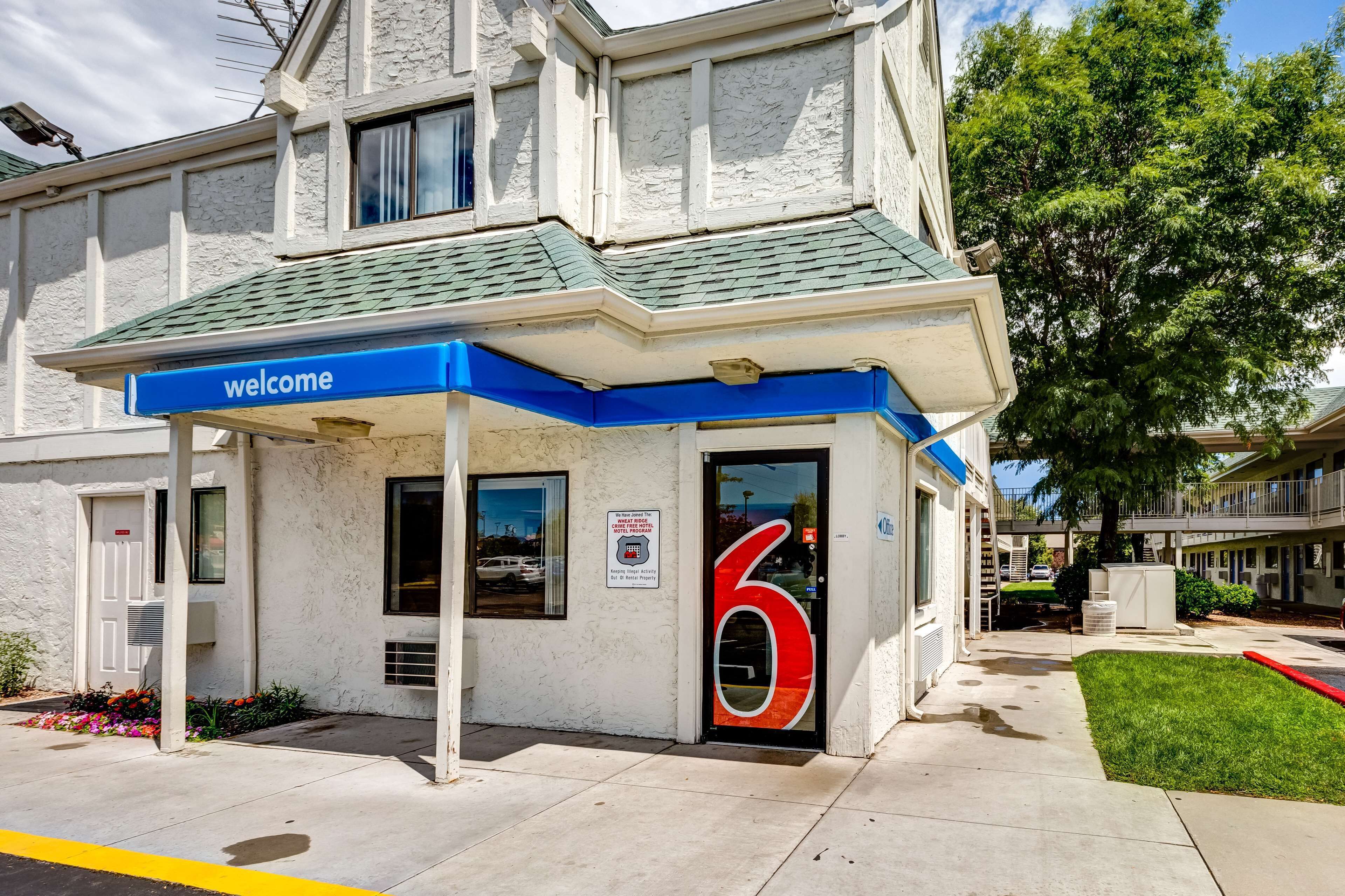A hotel entrance with a blue 'welcome' sign, a number '6' on the door, and a small garden area.
