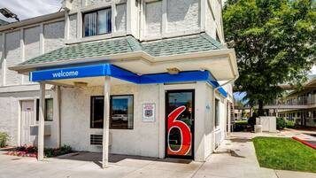 A hotel entrance with a blue 'welcome' sign, a number '6' on the door, and a small garden area.