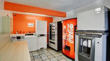 Una habitación con kitchenette, un refrigerador, una máquina expendedora y una pared con la marca Coca-Cola.
