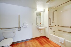 A bathroom with a toilet, sink, and bathtub, equipped with grab bars and a mirror. - Motel 6 Southington, CT - Hartford (Southington)