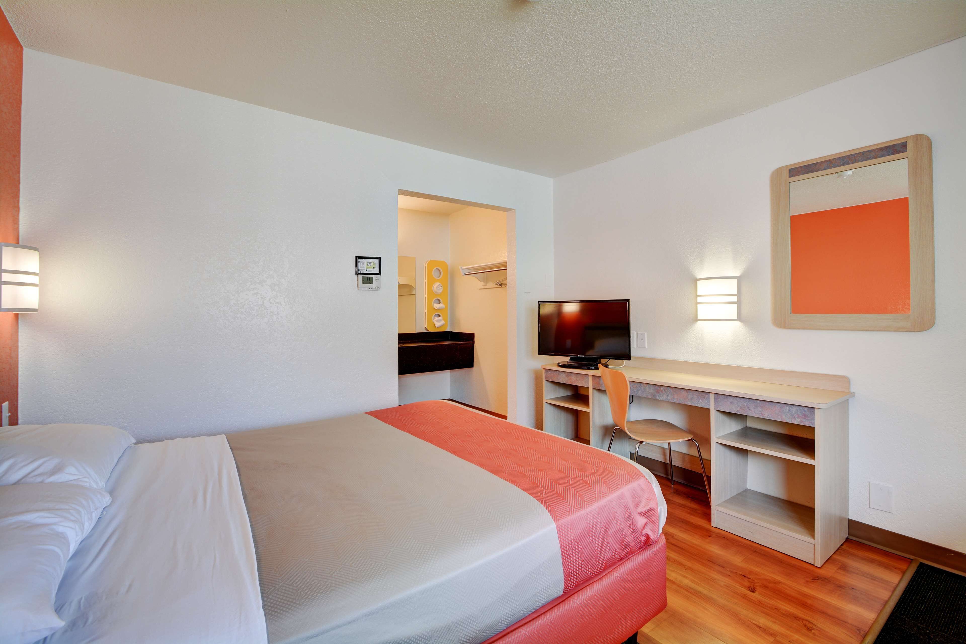 A hotel room with a bed, a desk with a chair, a television, and a mirror.
