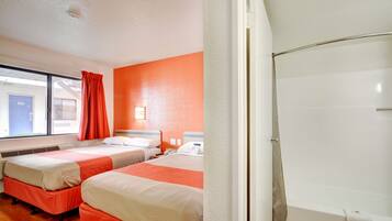 A hotel room with two beds, a window with curtains, a white bathtub, and a visible door.