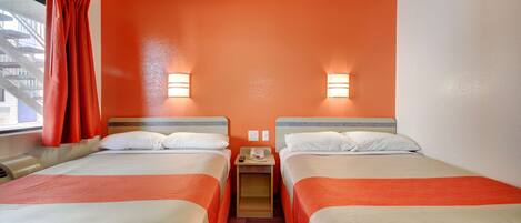 Een hotelkamer met twee bedden, oranje wanden en bedlampjes.