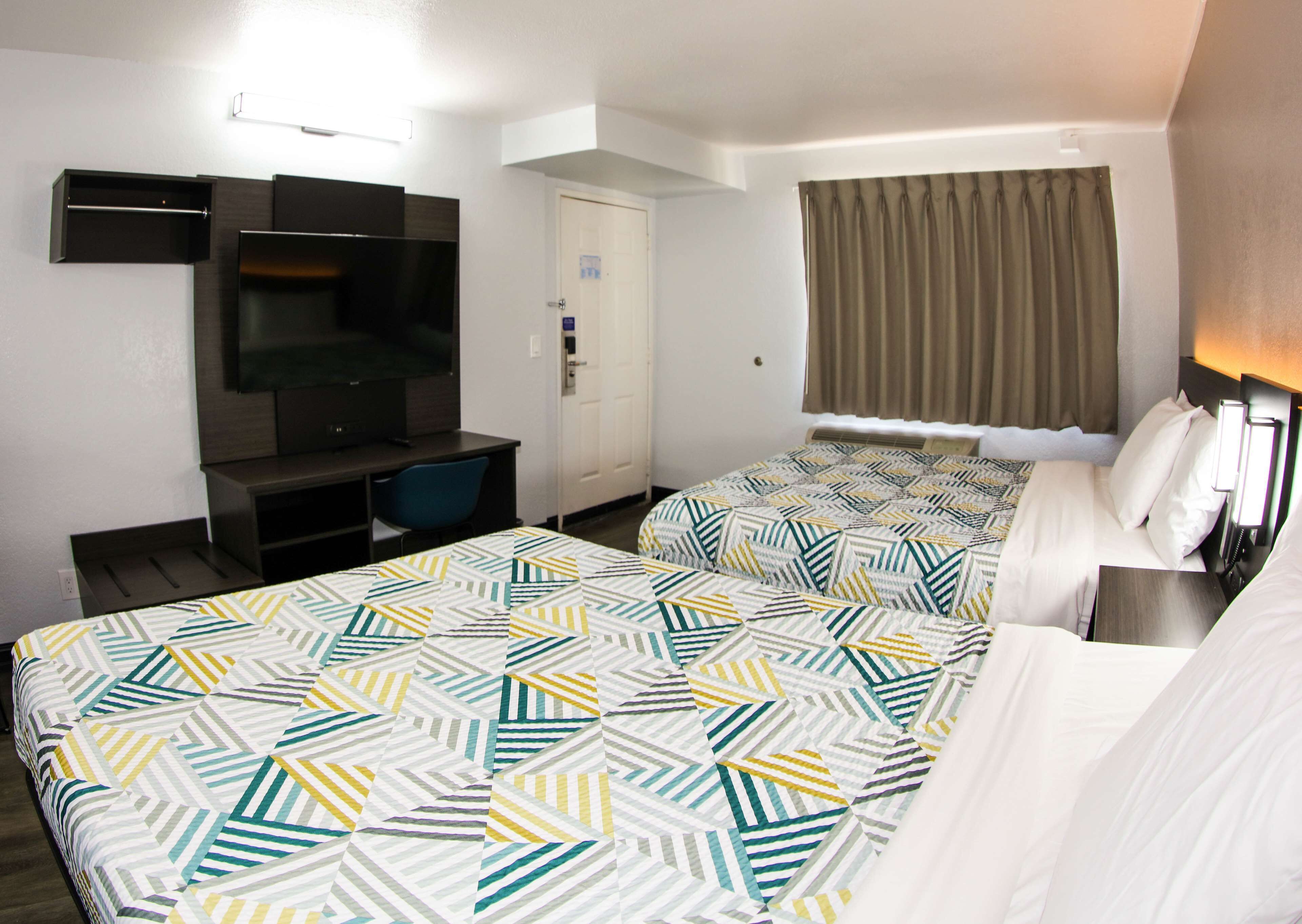 Habitación de hotel con dos camas, televisión, escritorio y ventana con cortinas.