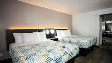 A hotel room with two beds, a nightstand, a wall-mounted lamp, and a bathroom visible through an open door.