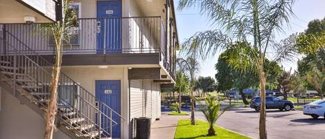 Un edificio de varios pisos con puertas azules, una escalera y un estacionamiento con coches.