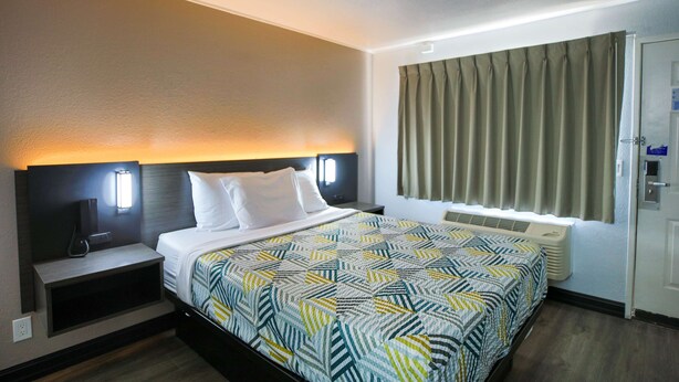 Una habitación de hotel con cama, mesitas de noche, lámpara y ventana con cortinas.