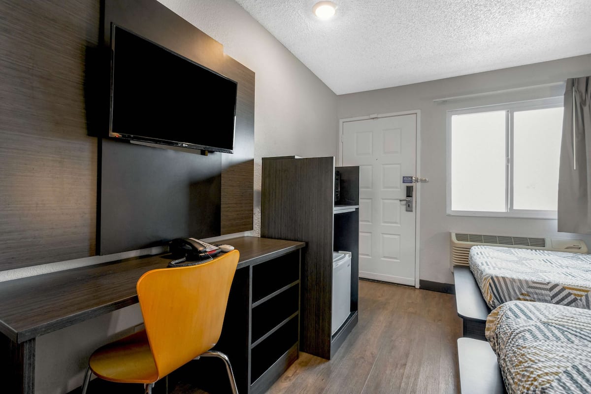 A hotel room with a desk, chair, TV, wardrobe, bed, and a window.