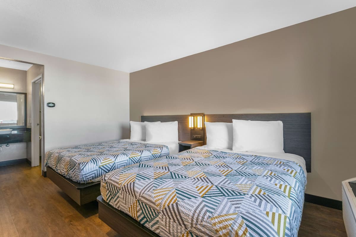 A hotel room with two beds, a nightstand, a wall-mounted lamp, and a bathroom door.