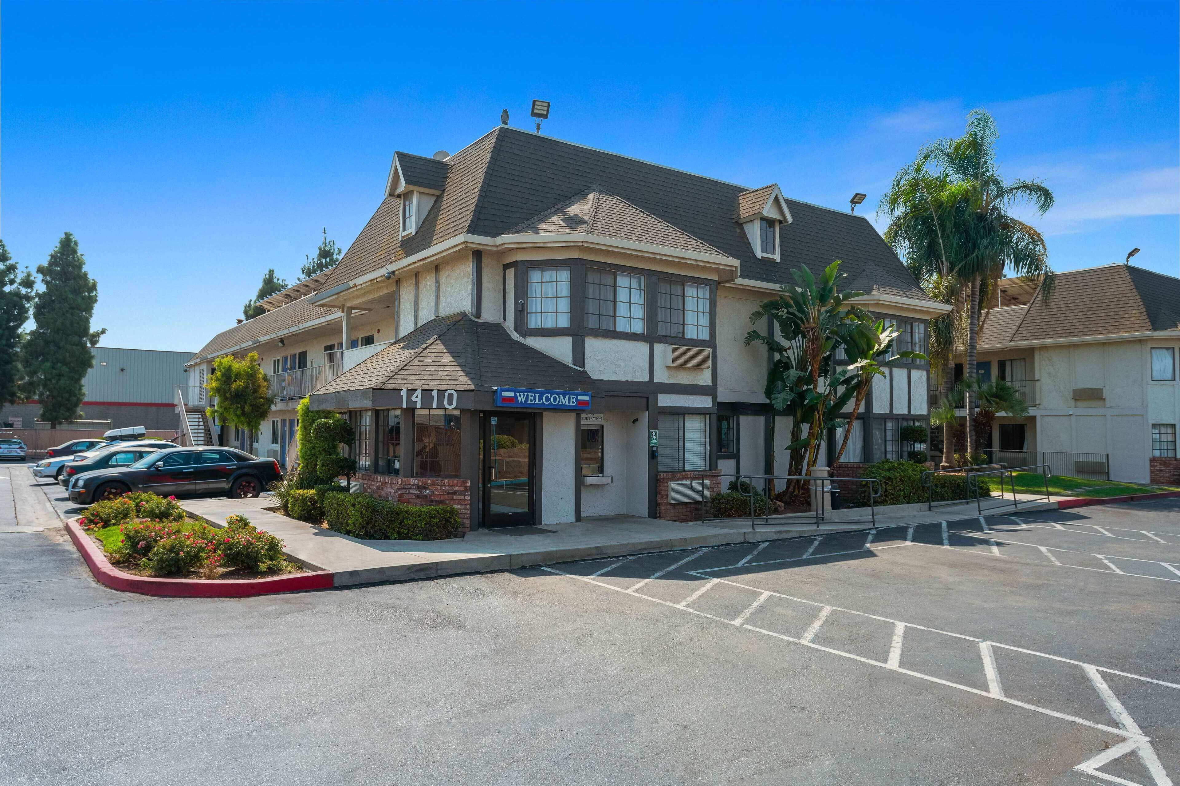 A hotel with a 'WELCOME' sign, a parking lot, and a row of parked cars.