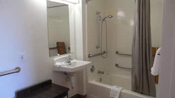 A bathroom with a sink, mirror, shower, and grab bars.
