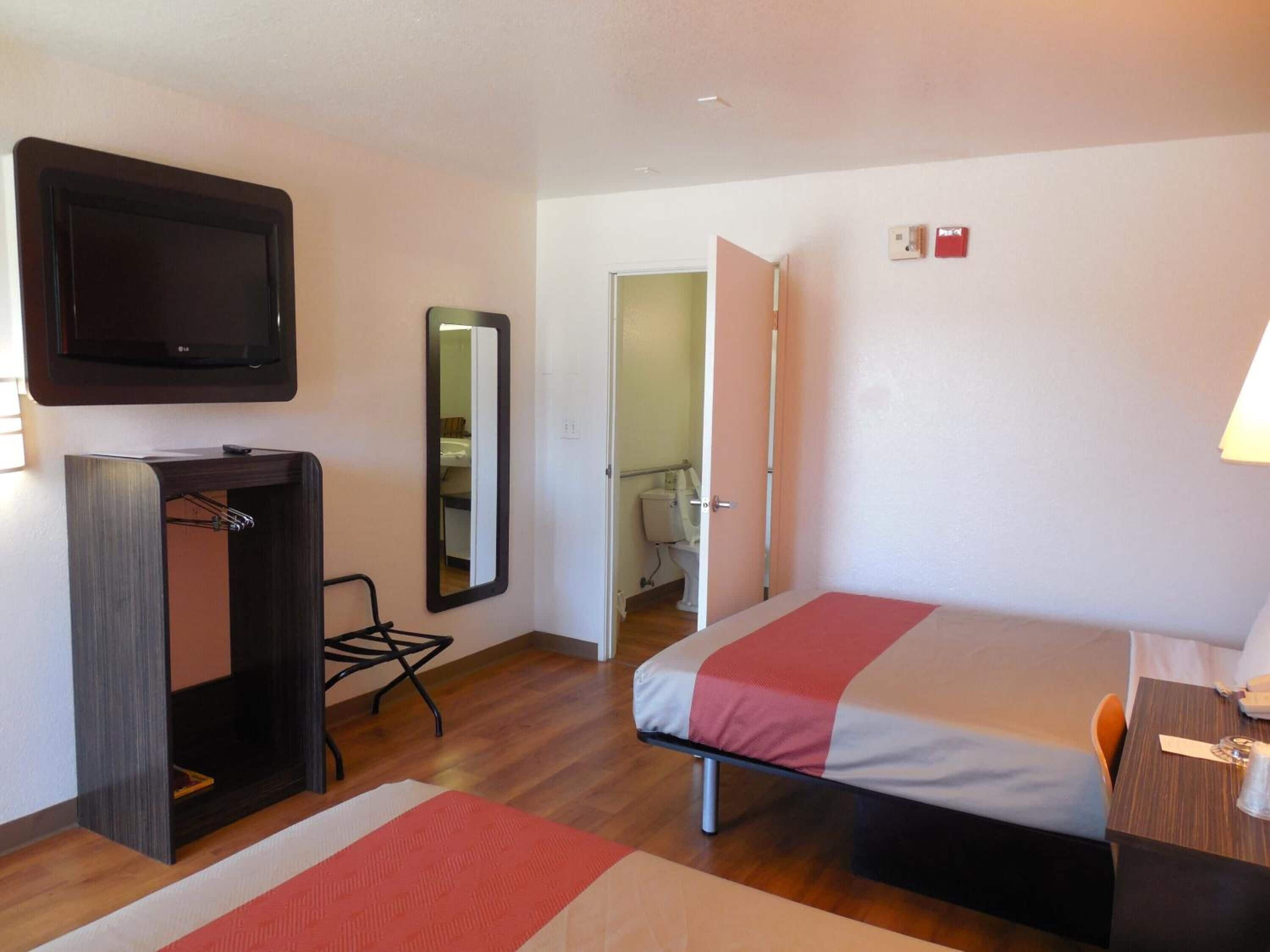 A hotel room with a bed, a desk, a TV, a mirror, and a wardrobe.