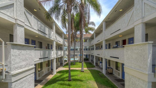 Un patio con piscina, palmeras y un edificio con varios balcones y ventanas.