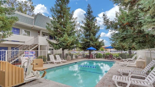 A swimming pool with lounge chairs and a no diving sign, surrounded by trees and a building with a staircase. - Motel 6 Rohnert Park, CA (Rohnert Park)