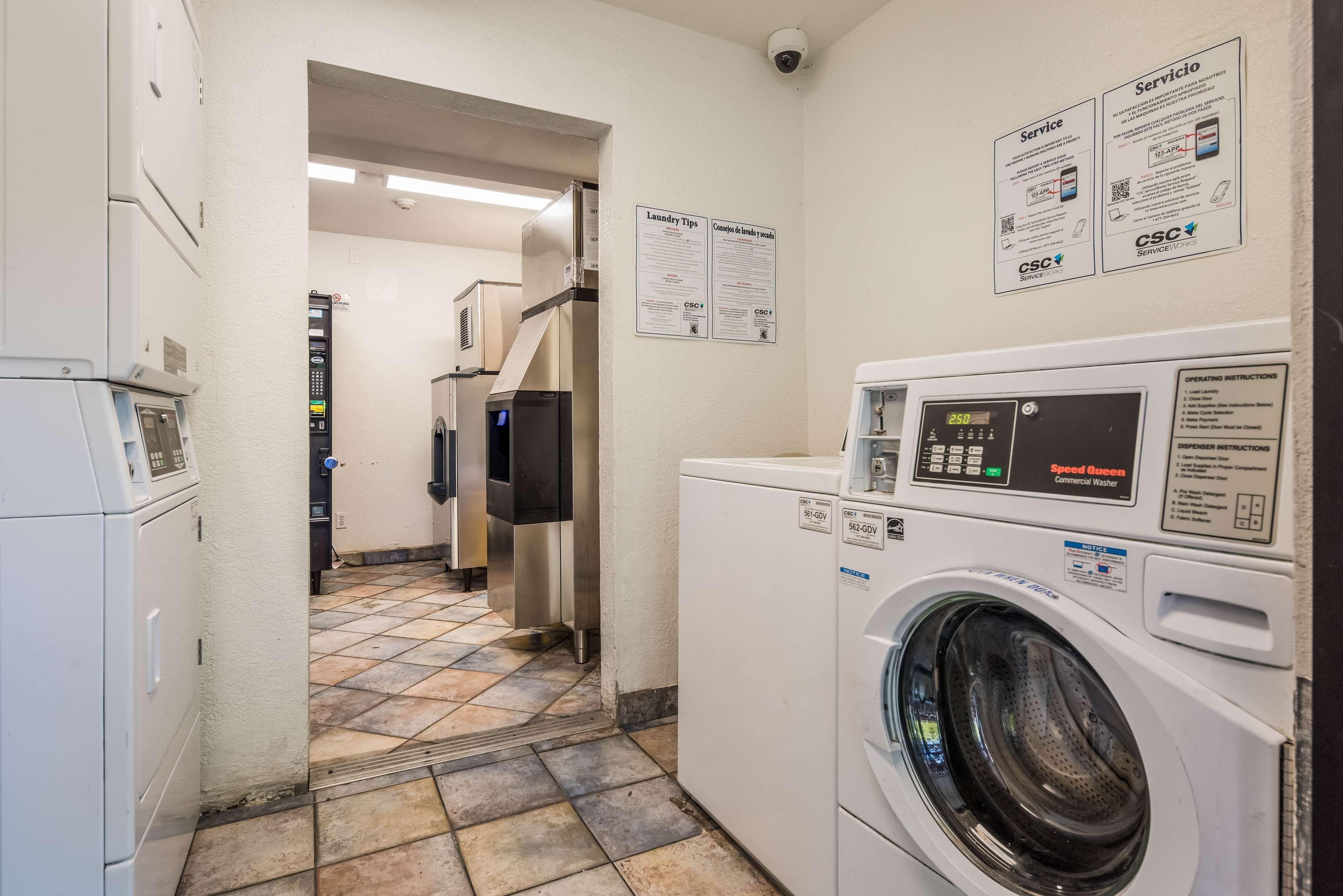 A laundry room with a Speed Queen commercial washer, a dryer, and a wall-mounted control panel.