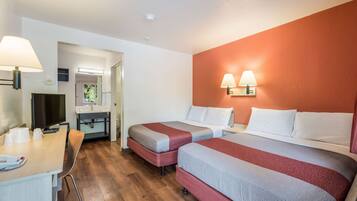 A hotel room with two beds, a desk with a lamp, a television, and a bathroom visible through an open door.