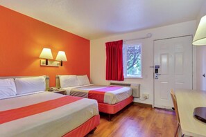 A hotel room with two beds, a window with red curtains, a white door, and a desk with a lamp.