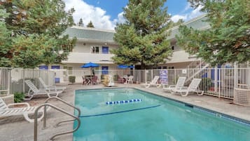 A swimming pool with lounge chairs and umbrellas, surrounded by a fence and trees.