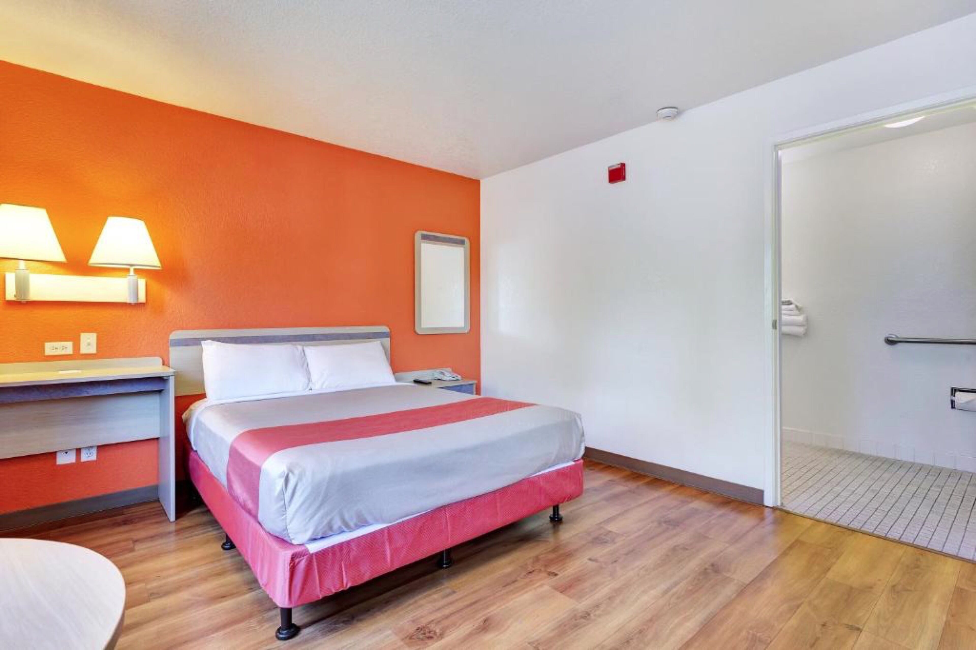 A hotel room with a bed, bedside table, lamp, and a door leading to a bathroom.