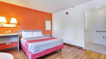 A hotel room with a bed, bedside table, lamp, and a door leading to a bathroom.