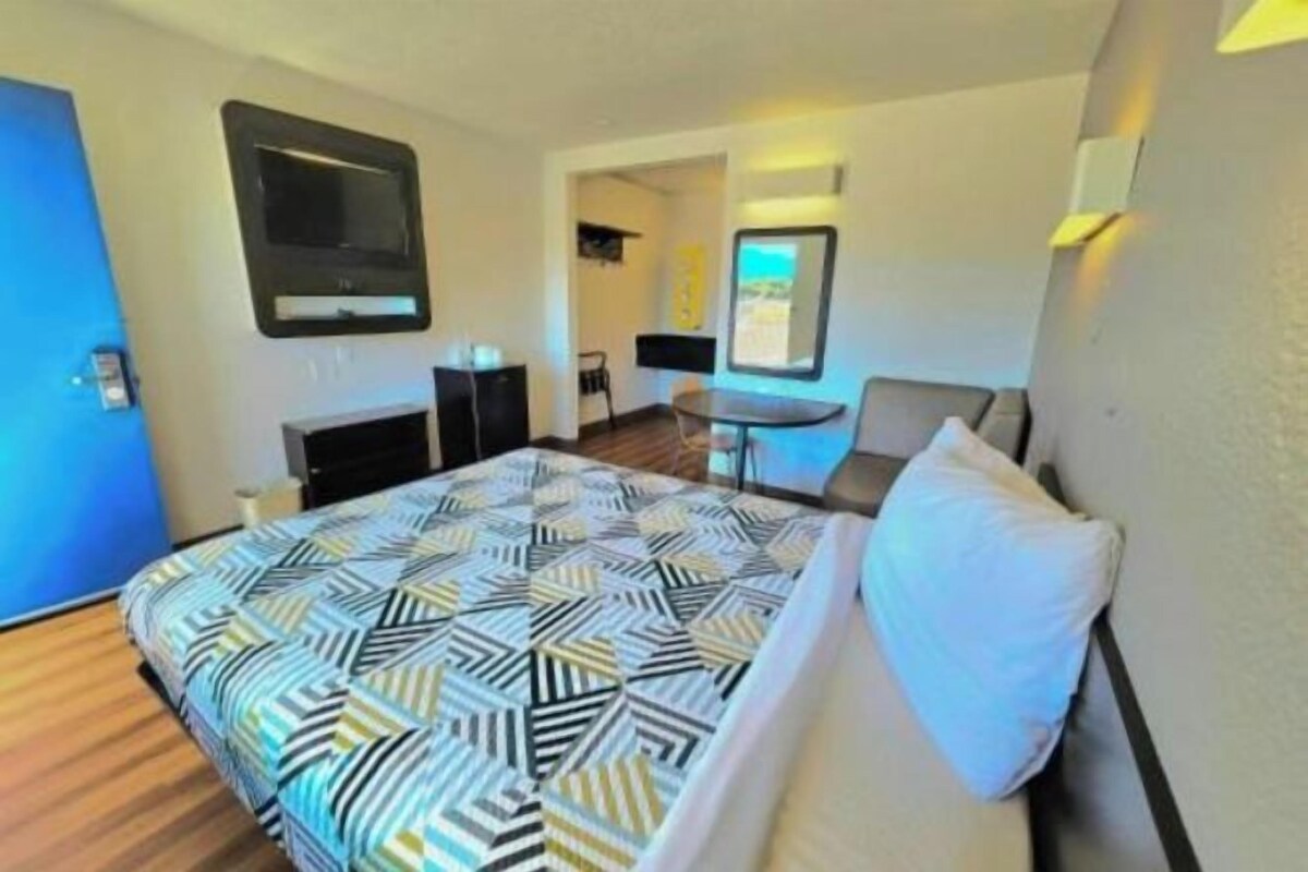 A hotel room with a bed, a desk, a chair, and a TV.