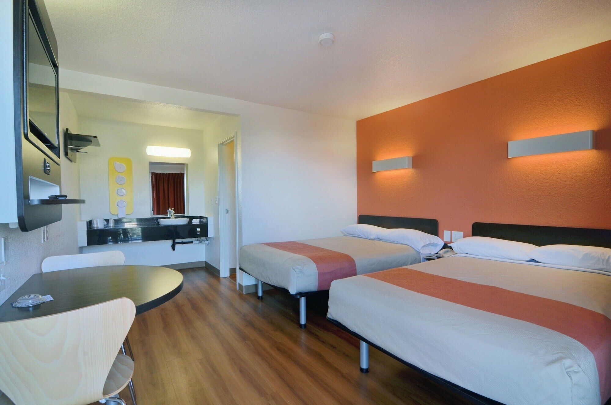 Habitación de hotel con dos camas, una mesita, una silla, un lavamanos y un espejo.