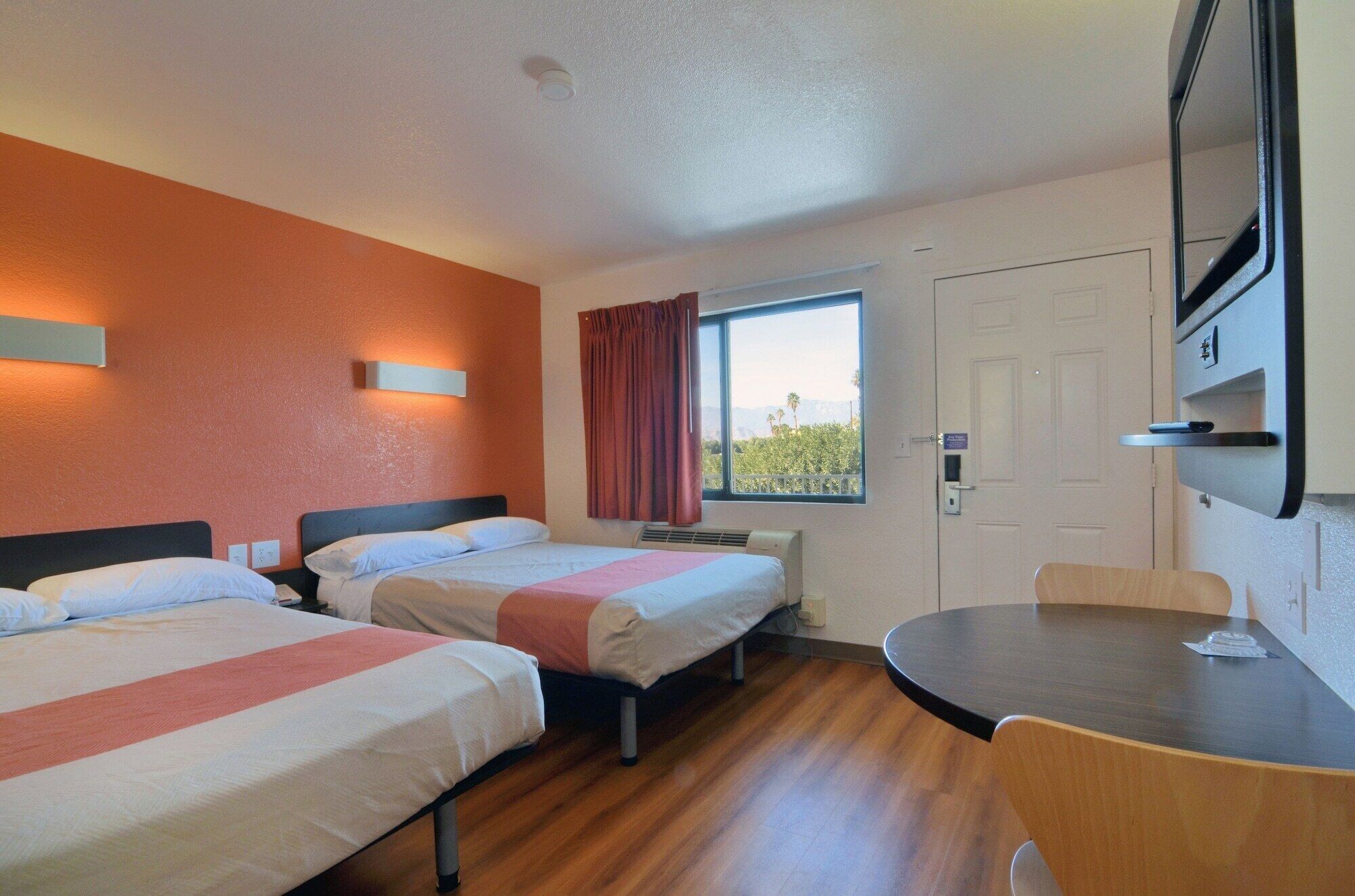 A hotel room with two beds, a dining table, and a window with a view.