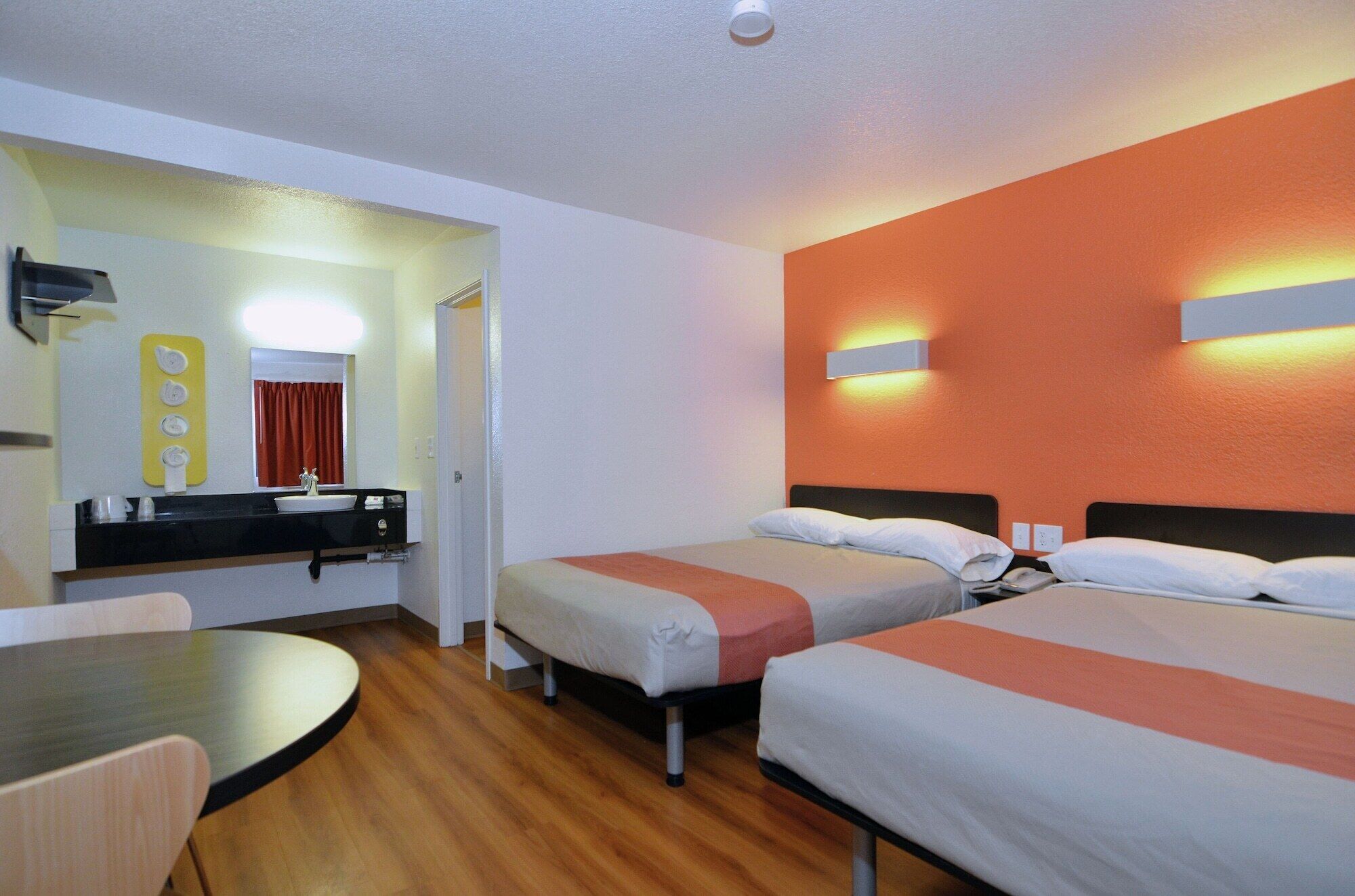 Une chambre d’hôtel avec deux lits, une petite table, un lavabo et un miroir.
