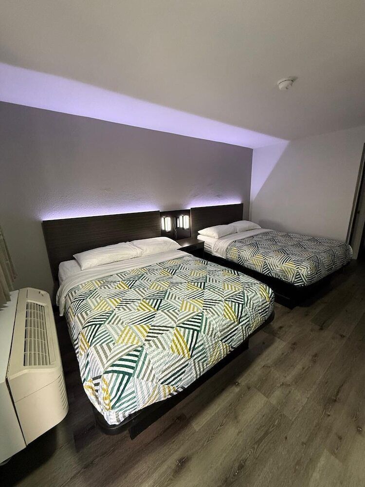 Una camera d'albergo con due letti, una lampada a soffitto e un condizionatore d'aria a parete.