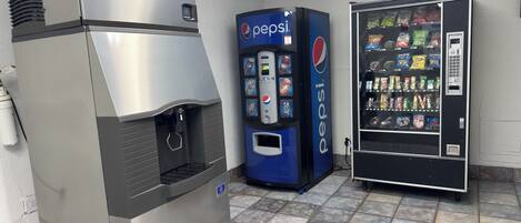 Zona de máquinas expendedoras con un dispensador de Pepsi y un refrigerador.