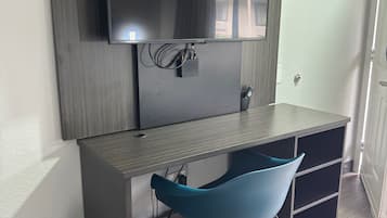 Una sala de estudio moderna con una televisión de pantalla plana grande montada en una pared de madera, un escritorio oscuro con cajones y una silla azul.