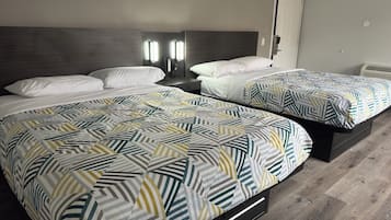 Une chambre d’hôtel avec deux lits, chacun recouvert d’une couvre-lit à motifs, une table de chevet avec une lampe et une porte dotée d’une poignée.