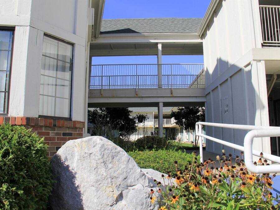 A multi-level building with a covered walkway and a stone feature in the foreground.